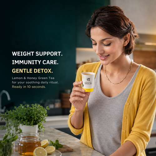 A woman in a kitchen holds a white and yellow cup of tea. Lifestyle image of HI TEA Lemon and Honey Green Tea Instant Cups, a warm and soothing green tea made for daily wellness, immunity care, digestion and weight-management routines. Just add hot water and enjoy in 10 seconds.